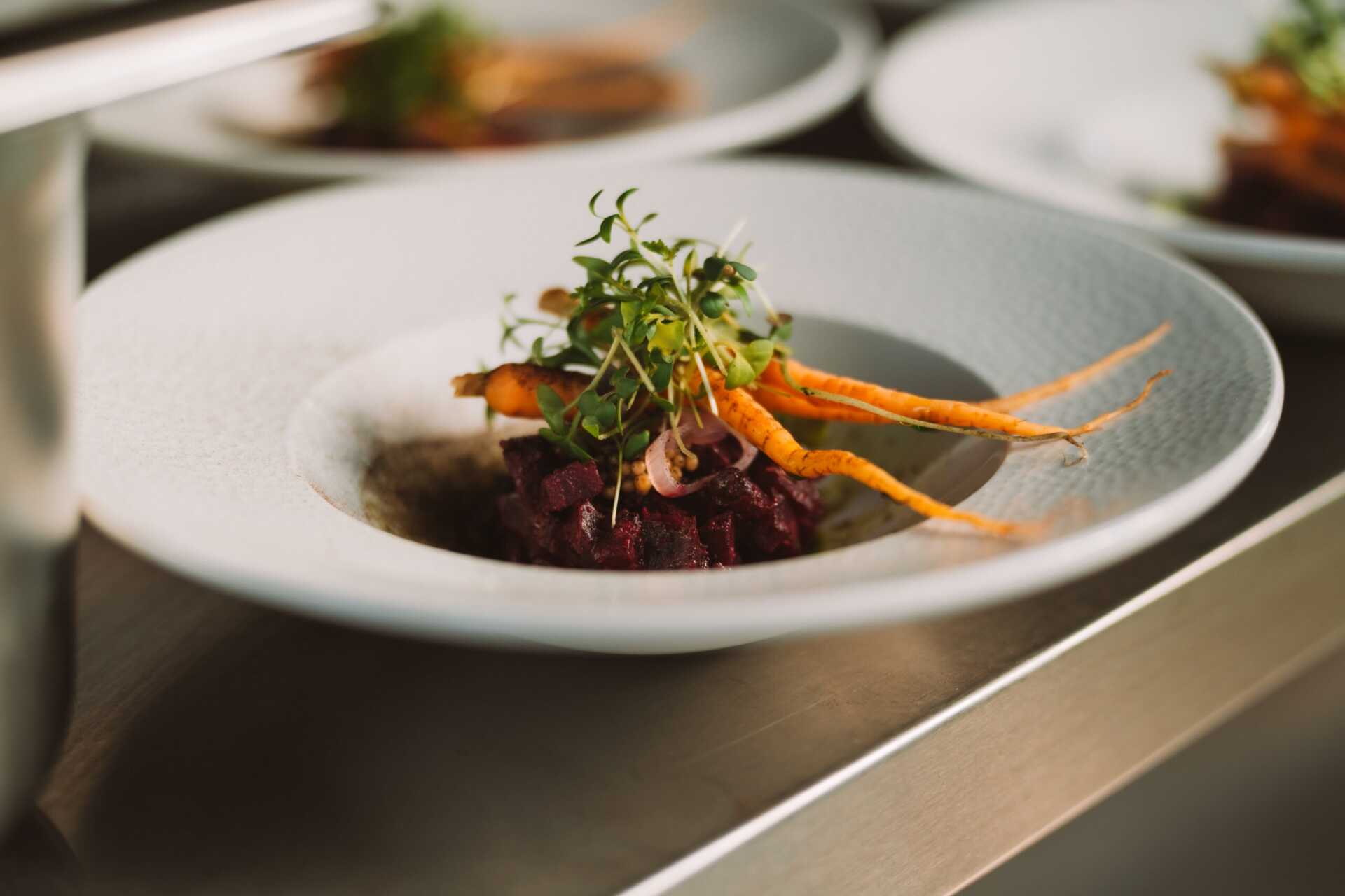 A plated main course of beef with glazed carrot and micro herbs